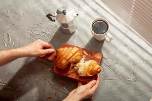 frühstück mit croissant auf schneidebrett und schwarzem kaffee. Morgenmahlzeit und Frühstückskonzept. foto