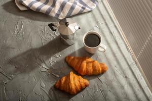 frühstück mit croissant auf schneidebrett und schwarzem kaffee. Morgenmahlzeit und Frühstückskonzept. foto
