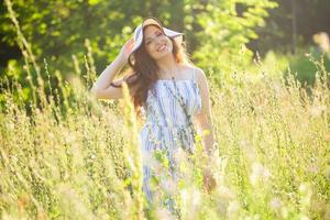 junge Frau, die an einem sonnigen Sommertag zwischen Wildblumen spazieren geht. Konzept der Freude an der Kommunikation mit der Sommernatur foto