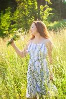 junge Frau, die an einem sonnigen Sommertag zwischen Wildblumen spazieren geht. Konzept der Freude an der Kommunikation mit der Sommernatur foto