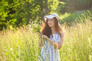 junge Frau, die am Sommerabend Blumen auf der Wiese pflückt foto