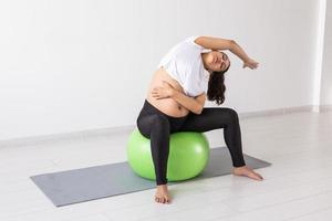 junge flexible schwangere Frau beim Turnen auf Teppich auf dem Boden auf weißem Hintergrund. das Konzept, den Körper auf eine leichte Geburt vorzubereiten foto