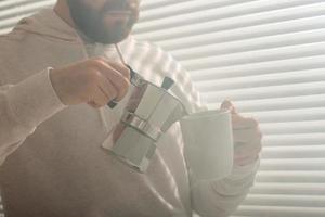 nahaufnahmeporträt des jungen stilvollen hipster-mannes, der am sommertag kaffee im büro gießt. konzept des belebenden morgens und der positiven stimmung foto