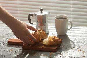 frühstück mit croissant auf schneidebrett und schwarzem kaffee. Morgenmahlzeit und Frühstückskonzept. foto