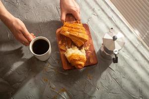 frühstück mit croissant auf schneidebrett und schwarzem kaffee. Morgenmahlzeit und Frühstückskonzept. foto