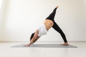 junge flexible schwangere Frau beim Turnen auf Teppich auf dem Boden auf weißem Hintergrund. das Konzept, den Körper auf eine leichte Geburt vorzubereiten foto