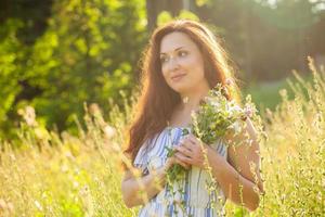 junge Frau, die an einem sonnigen Sommertag zwischen Wildblumen spazieren geht. Konzept der Freude an der Kommunikation mit der Sommernatur foto