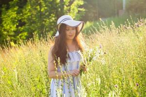 junge Frau, die am Sommerabend Blumen auf der Wiese pflückt foto