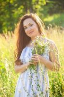 junge Frau, die an einem sonnigen Sommertag zwischen Wildblumen spazieren geht. Konzept der Freude an der Kommunikation mit der Sommernatur foto