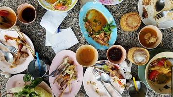 Flaches thailändisches Essen mit würzigem Papayasalat, weißen Nudeln, Knochenhuhn, Krabbensalat, Sauce und frischen Tomaten bleiben nach dem Mittagessen im Restaurant auf dem Tisch. Konzept der Lebensmittelverschwendung. foto