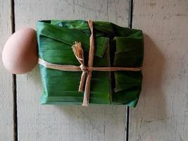 Blick von oben auf gekochtes Ei und Reis, eingewickelt in Bananenblätter auf weißem Holzhintergrund. Flache Essenslage auf Hartholzplatte. Mittagessen und verwenden Sie natürliches Material anstelle von Plastik, Schaumstoffbox oder Teller. foto