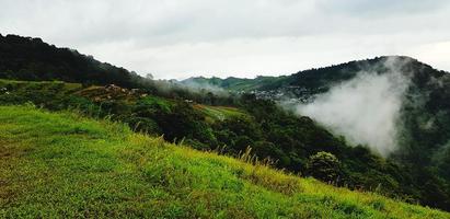 schöne reihe von grünen bergen, weißen wolken, kleinem dorf und nebel am morgen mit kopienraum. landschaftsansicht des hügels in phetchabun, thailand. natürliche Tapete und berühmter Ort für Reisen. foto