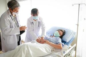 Zwei asiatische Ärzte untersuchten die Bauchschmerzen einer Frau, die in einem Krankenhausbett lag. Behandlung von Patienten während der Coronavirus-Epidemie. Konzept des medizinischen Dienstes foto