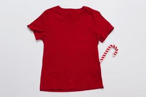 Schließen Sie herauf rotes leeres Schablonent-shirt mit Kopienraum. weihnachtsferienkonzept. Draufsichtmodell-T-Shirt. Feiertagsdekorationen weißer Hintergrund. frohes neues jahr zubehör. Weihnachts-Outfit. selektiver Fokus foto