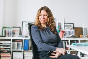 charmante lächelnde erwachsene frau mittleren alters mit lockigem haar architekt-designer-manager, der in einem hellen, modernen büro arbeitet foto