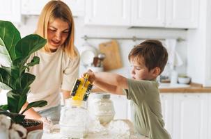 junge Frau Mutter und ihr kleiner Sohn haben Spaß beim Kochen mit Mehl am Tisch in der Küche zu Hause. Junge spielt mit Autospielzeug foto