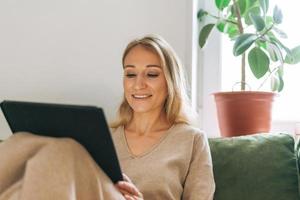 schöne blonde junge Künstlerin Illustratorin Zeichnung auf Tablette in der Nähe des Fensters zu Hause foto