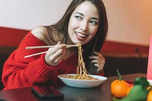 schöne lächelnde junge asiatin in roter kleidung, die asiatisches essen mit bambusstäbchen im chinesischen vietnamesischen restaurant isst foto