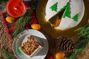 traditioneller weihnachtskuchen oder pudding, auf dem hintergrund von weihnachtsdekorationen, draufsicht auf ein stück kuchen auf einem teller. Stillleben mit Weihnachtsessen mit Obst englischer Kuchen mit Marzipan. foto