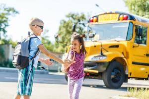 Schönes kleines Schulmädchen mit Klassenkameraden in der Nähe des Schulbusses foto