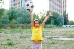 Outdoor-Foto von niedlichen kleinen Mädchen, die sich auf Fußball im grünen Gras lehnen foto