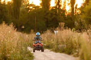 Ein kleiner Junge, der einen Helm trägt, fährt mit einem Quad am Ufer eines Gebirgsflusses. foto