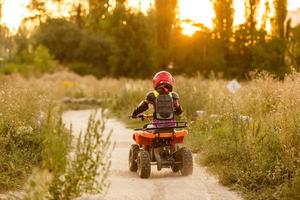 das kleine mädchen fährt ein quad atv. Ein Mini-Quad ist ein cooles Mädchen mit Helm und Schutzkleidung. Elektro-Quad-Elektroauto für Kinder macht grüne Technologie populär. foto