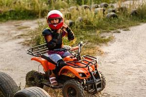 das kleine mädchen fährt ein quad atv. Ein Mini-Quad ist ein cooles Mädchen mit Helm und Schutzkleidung. Elektro-Quad-Elektroauto für Kinder macht grüne Technologie populär. foto