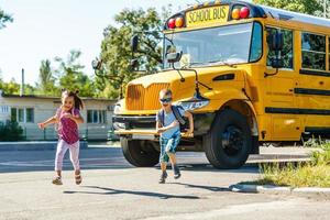 Schönes kleines Schulmädchen mit Klassenkameraden in der Nähe des Schulbusses foto