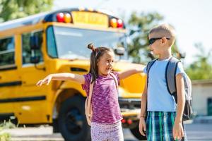 Schönes kleines Schulmädchen mit Klassenkameraden in der Nähe des Schulbusses foto