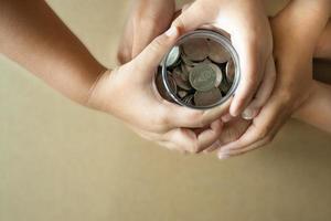 Kinderhände, die Münzen in einem Glas zusammenhalten, als Sparkonzept für Familie oder Bildung. foto