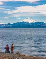 Fischer mit Angelrute an der Küste des Pazifischen Ozeans im Hintergrund des Vulkans foto