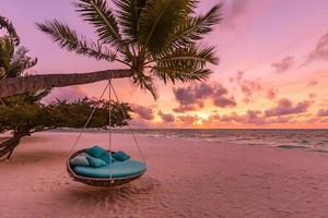 romantischer sonnenuntergang am strand. Palme mit Schaukel, die vor dem majestätischen Wolkenhimmel hängt. Traumnaturlandschaft, tropisches Inselparadies, Reiseziel für Paare. liebe küste, nahaufnahme seesand. Entspannen Sie sich am unberührten Strand foto