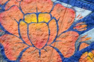 Fragment von Graffiti-Zeichnungen. Die alte Wand ist mit Farbflecken im Stil der Straßenkunstkultur dekoriert. orangene Blume foto