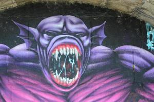 Fragment von Graffiti-Zeichnungen. Die alte Wand ist mit Farbflecken im Stil der Straßenkunstkultur dekoriert. Lila gruseliges Monster foto