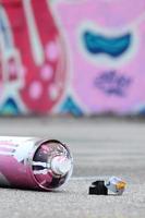 mehrere gebrauchte sprühdosen mit rosa und weißer farbe und kappen zum sprühen von farbe unter druck liegen auf dem asphalt in der nähe der bemalten wand in farbigen graffiti-zeichnungen foto