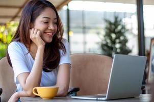 asiatische frau, die ein weißes trägt, das in einem café sitzt. eine pause von der arbeit machen, kaffee trinken entspannt glücklich lächeln. foto