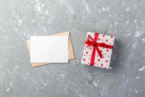 Umschlagpost mit rotem Herzen und Geschenkbox über grauem Zementhintergrund. valentinstagkarte, liebes- oder hochzeitsgrußkonzept foto