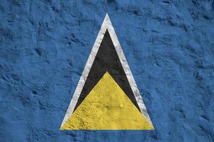 st. lucia-flagge in hellen farben auf alter reliefputzwand dargestellt. strukturierte Fahne auf rauem Hintergrund foto