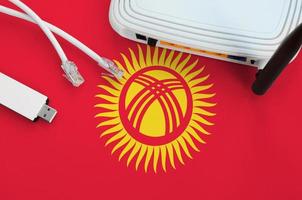 kirgisistan-flagge auf tisch mit internet-rj45-kabel, drahtlosem usb-wlan-adapter und router. Konzept der Internetverbindung foto