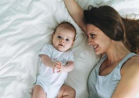 junge mutter, die spaß mit niedlichem babymädchen auf bett hat, natürliche töne, liebesgefühl foto