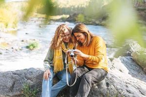 junge reisende freunde, die fotos vor der kamera auf dem hintergrund der berge und des flusses machen und in der herbstnatur wandern