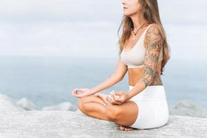 Junge, fitte, schöne Frau mit langen Haaren in weißer Sportkleidung praktiziert Yoga und Meditation am Meeresstrand foto