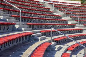 leere rote Plastikstühle auf den Tribünen des Stadions oder Amphitheaters. viele leere Zuschauerplätze auf den Tribünen. foto