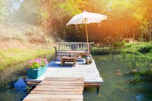 Sitzbank auf der Terrasse Garten und Holzbrücke Gehweg am Wasserteich und Tisch mit Sonnenschirm im Sommer foto