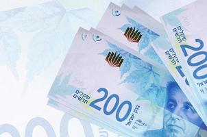 200 israelische neue Schekel-Scheine liegen im Stapel auf dem Hintergrund einer großen halbtransparenten Banknote. abstrakte Darstellung der Landeswährung foto