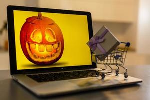 Wagen voller Geschenke für Halloween in der Nähe eines Kürbises. Kürbis in einem Laptop foto