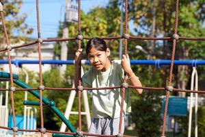 asiatisches Mädchen, das Kletterseilnetz auf dem Spielplatz spielt. konzept spielplatz, kindliche entwicklung, sport und erholung. weicher und selektiver Fokus. foto