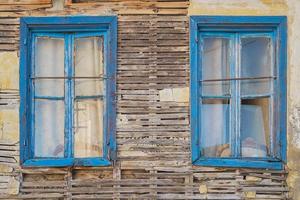 Fassade eines bröckelnden alten Holzhauses mit blauen Fenstern. verlassene häuser der alten stadtidee für hintergrund foto