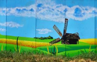 die alte Mauer, gemalt in Graffiti-Farbzeichnung mit Aerosolfarben. ein bild einer traditionellen ukrainischen landschaft mit sonnenblumen, kalina und einer mühle auf einem feld foto